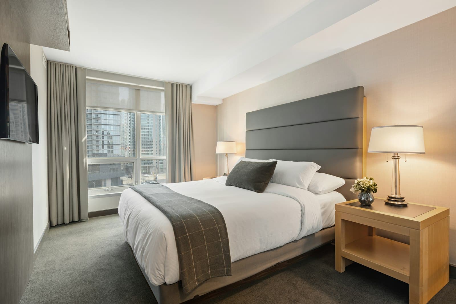 A city hotel-style bedroom with a dressed bed and tall windows