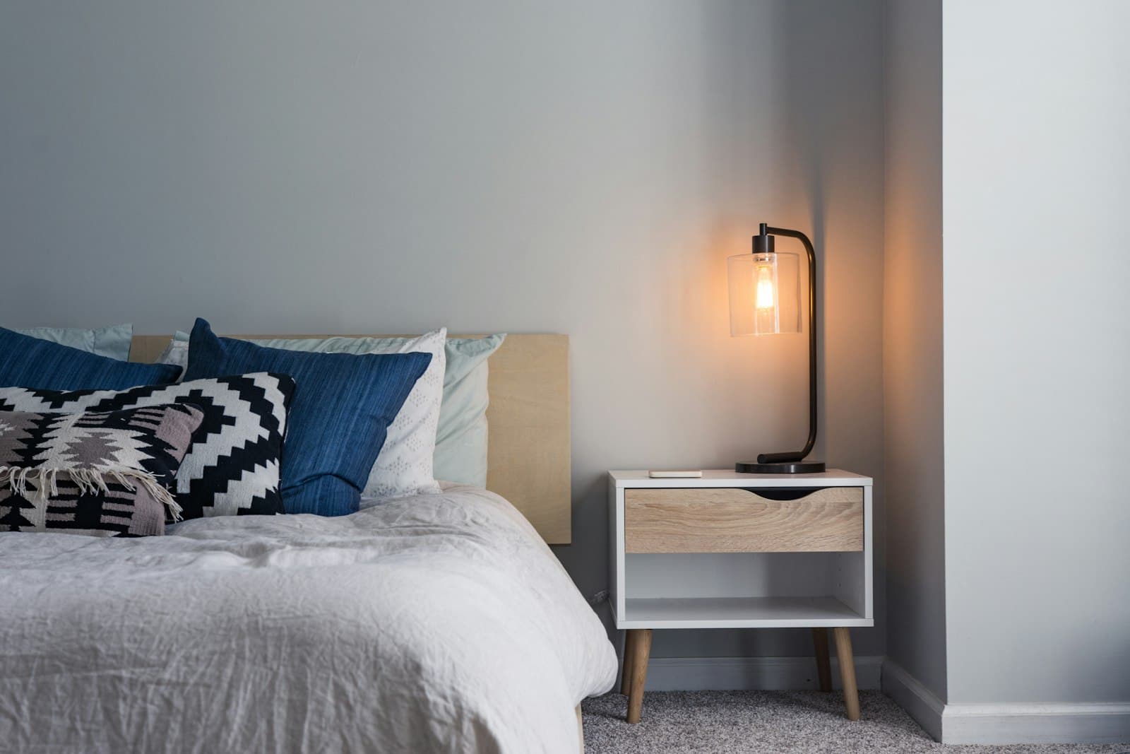 A made bed with layered pillows and a warm bedside lamp