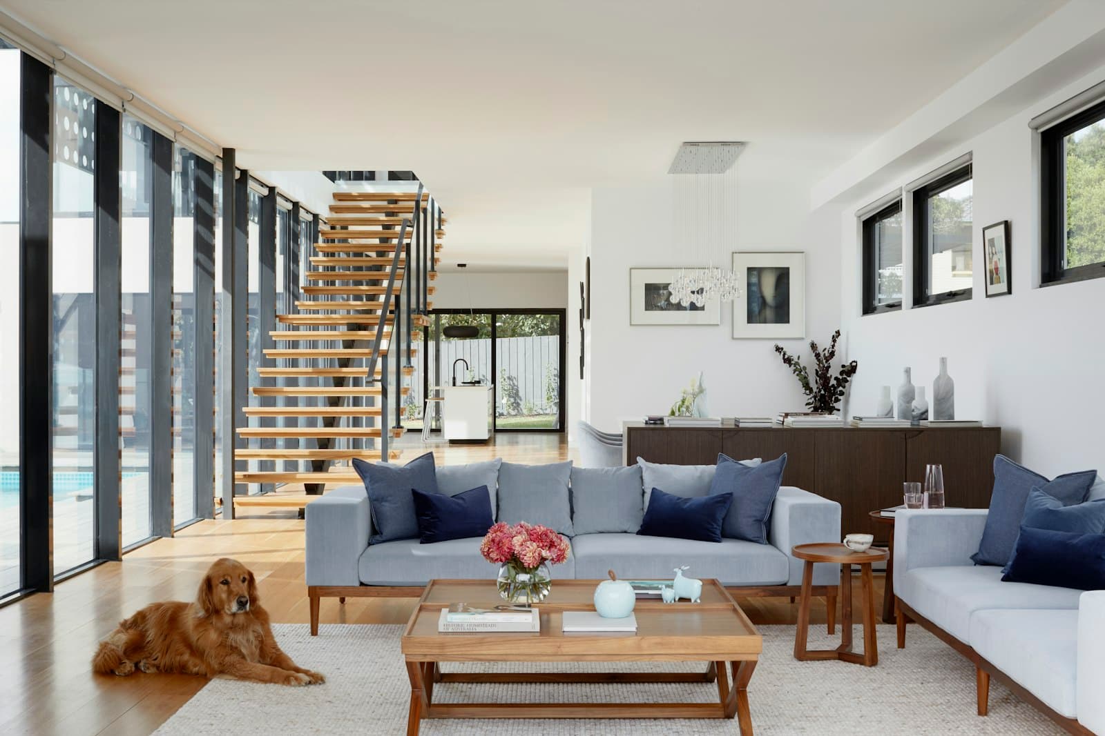 A sunlit living room with a timber staircase and long windows